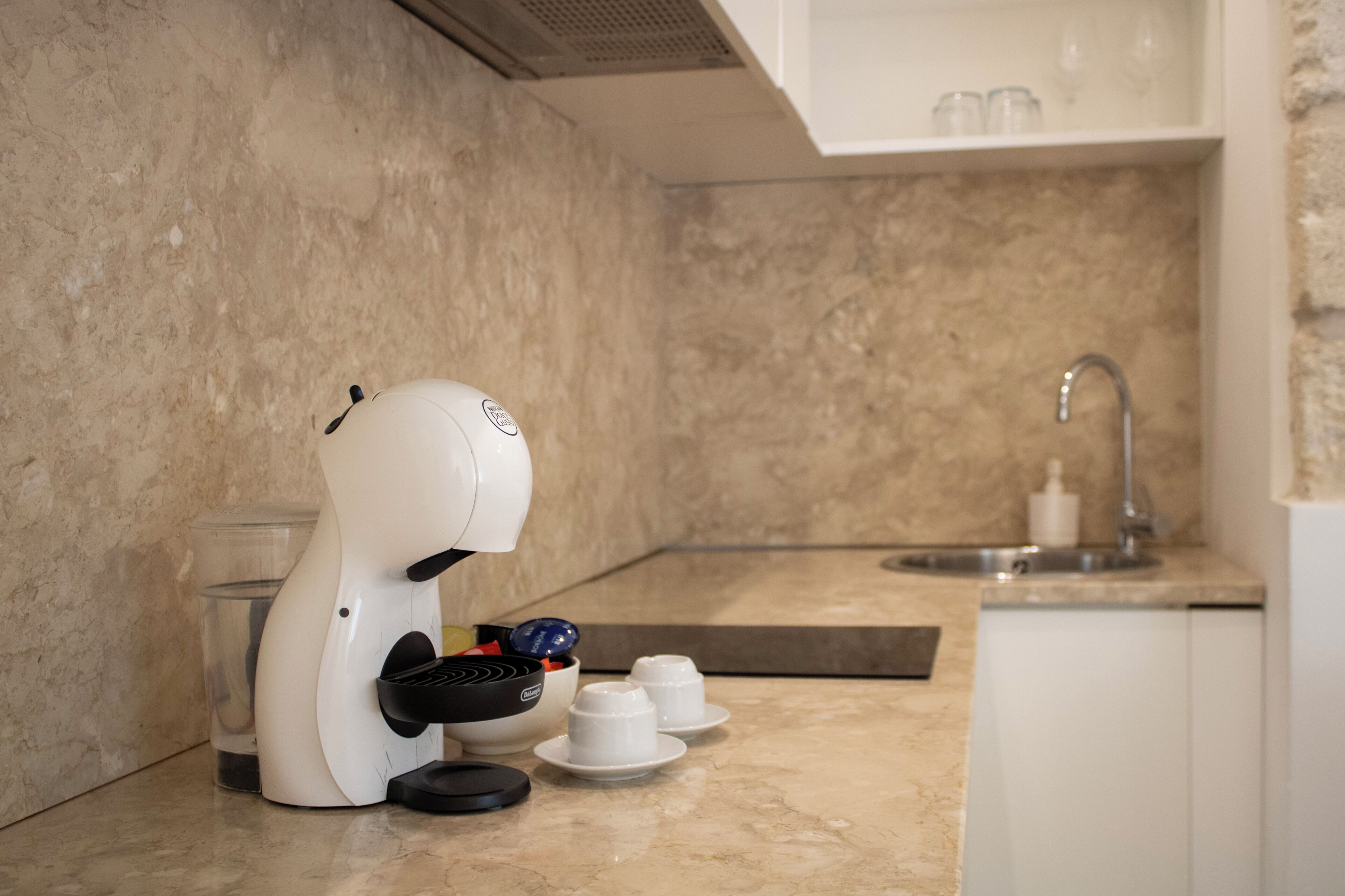 Una cocina con cafetera, lavamanos y encimera de mármol.