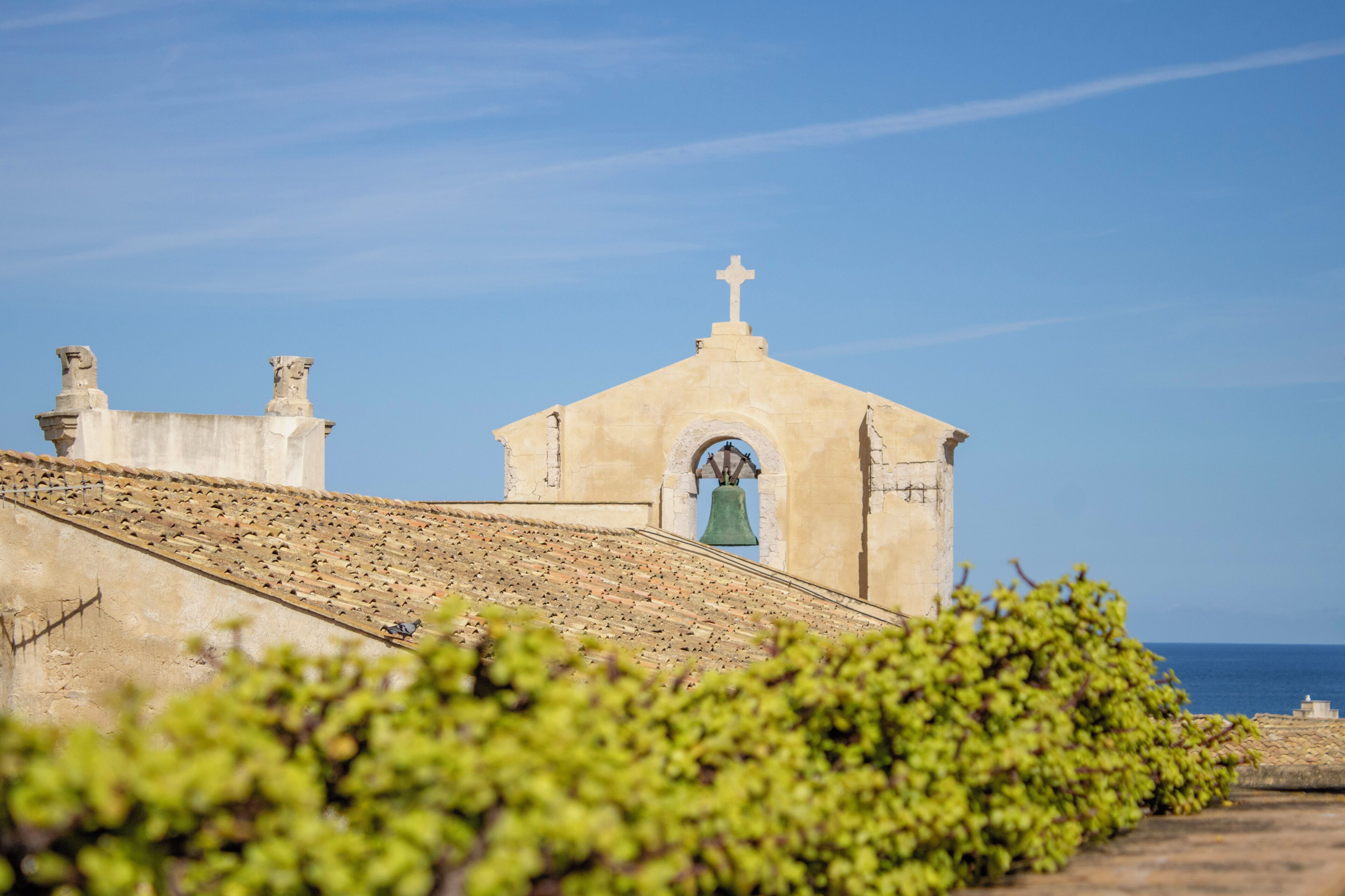 A church with a bell tower and a clear view of the sea.