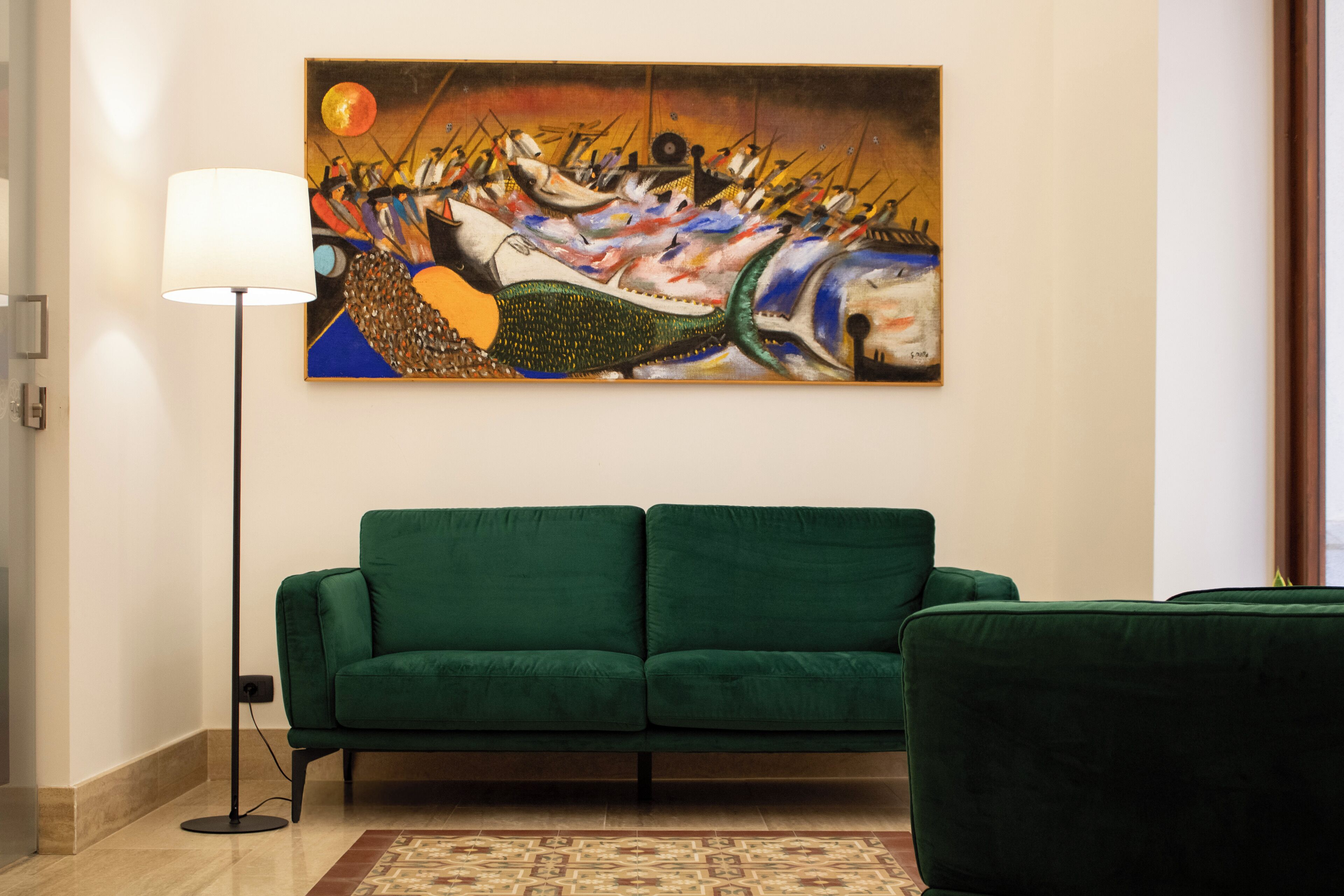 A living room with a green sofa, a floor lamp, and a painting on the wall.