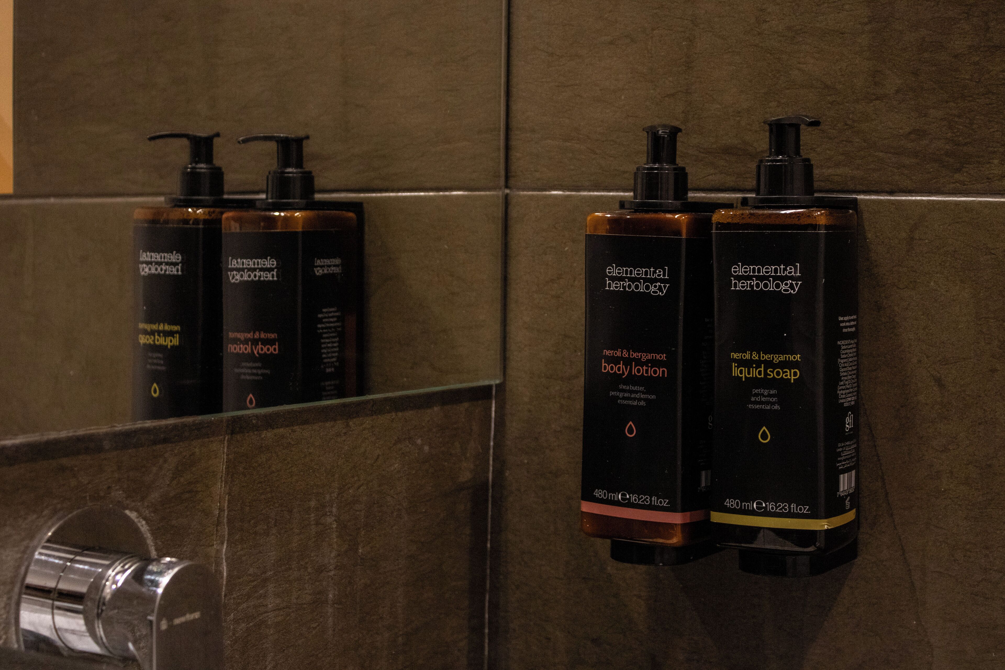 Ein Badezimmer mit einem Spiegel, der drei Tiegel Körperlotion und zwei Flaschen Flüssigseife reflektiert.