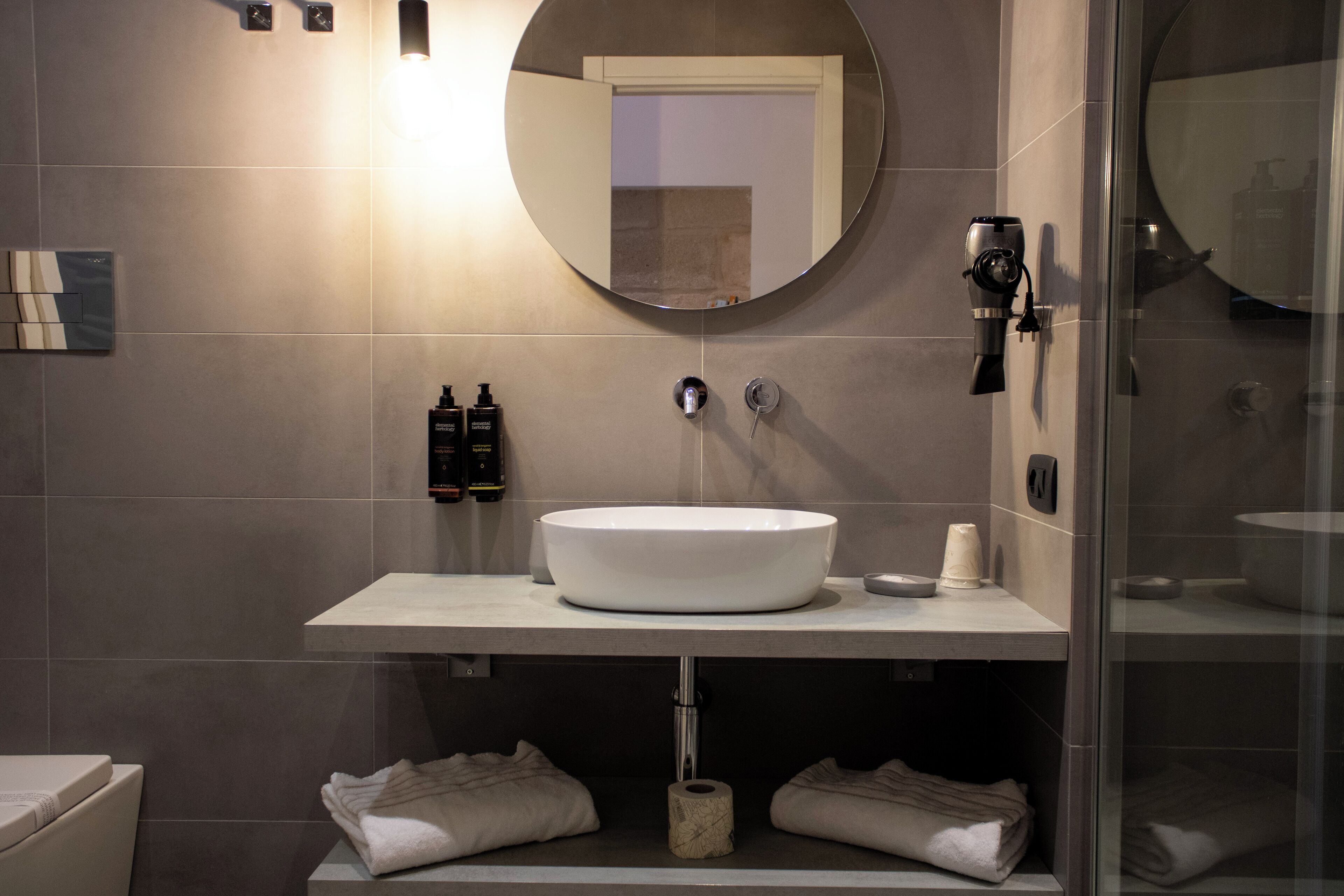 Une salle de bain moderne avec un miroir rond, un lavabo blanc et un porte-serviettes.