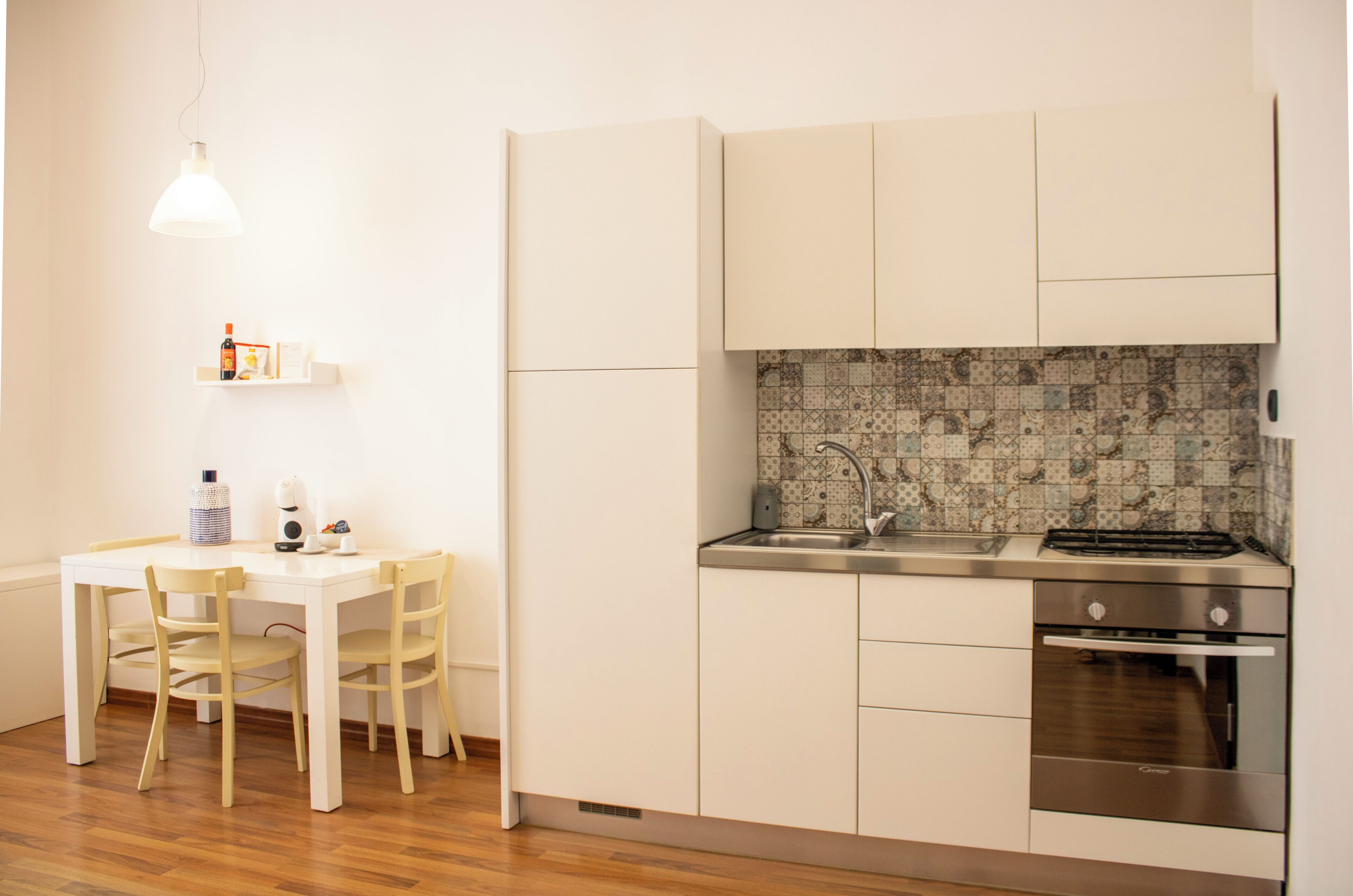 A compact kitchen with white cabinets, a tiled backsplash, a stainless steel sink, and an oven.