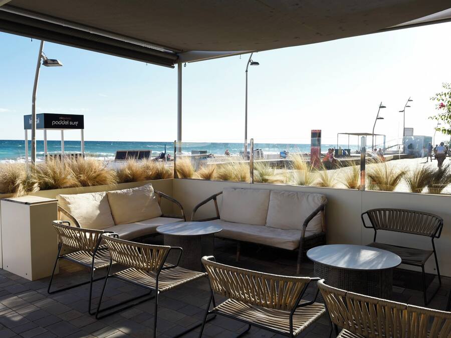 Eine Terrassensitzgelegenheit am Strand mit einer Couch, Stühlen und einem Tisch, mit Blick auf den Ozean.