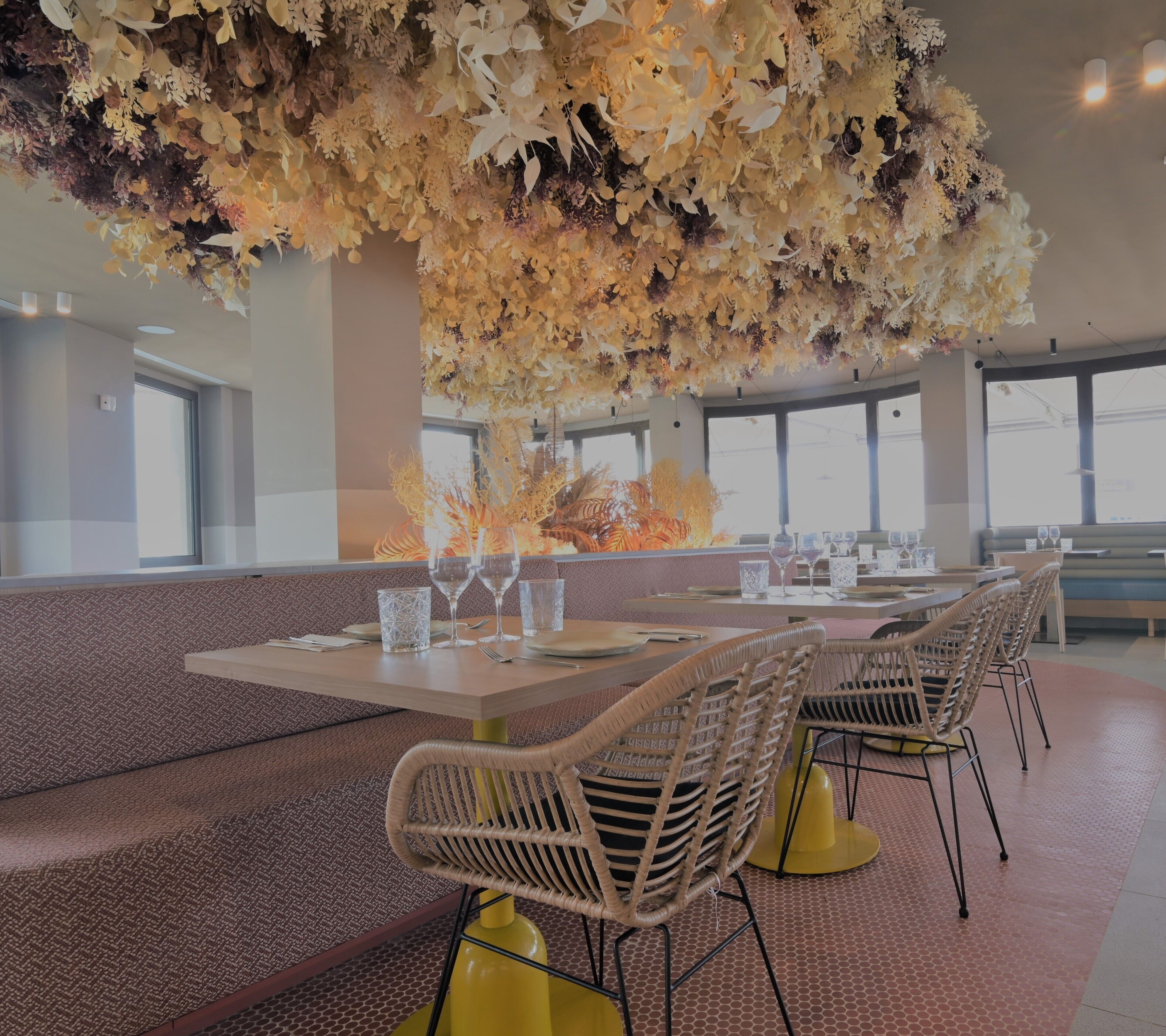 Un restaurante con techos altos, ventanas amplias y un arreglo floral central. Las mesas están dispuestas con sillas y copas de vino.