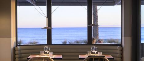Comedor con vista al océano, con asientos acolchados y mesas.