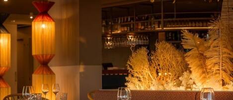 Een restaurantinterieur met gedekte tafels, een bar met flessen en decoratieve planten.