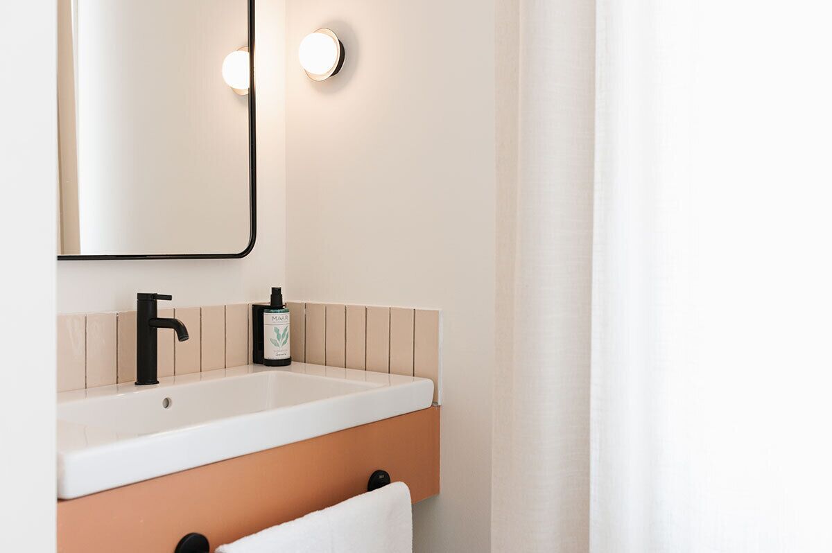 Een badkamer met een witte wastafel, een zwarte kraan en een spiegel met twee wandlampen.