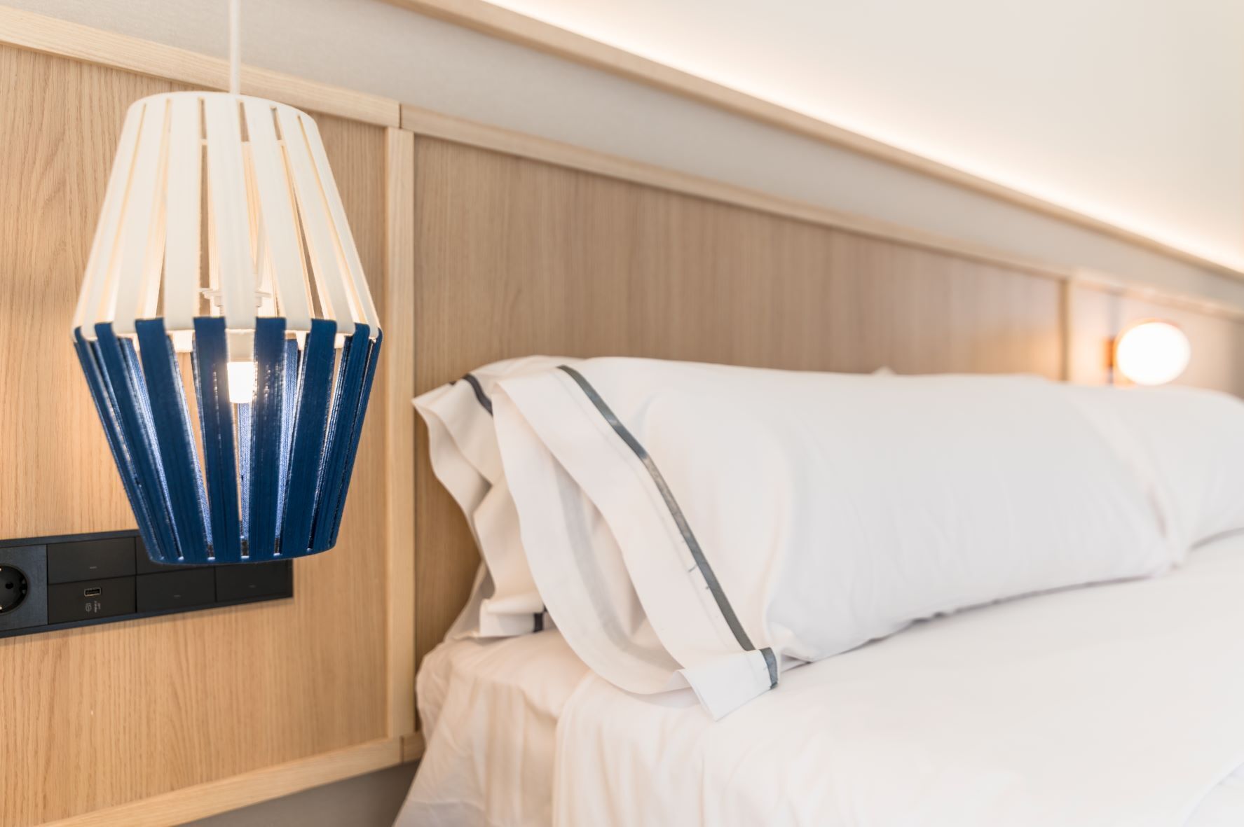 A hotel room with a bed, a wooden panel wall, and a blue pendant light.