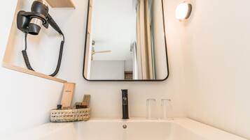 Un baño con lavamanos blanco, un espejo, secador de pelo y lámpara.