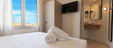 A hotel room with a bed, a TV mounted on the wall, a mirror, and a window with curtains.