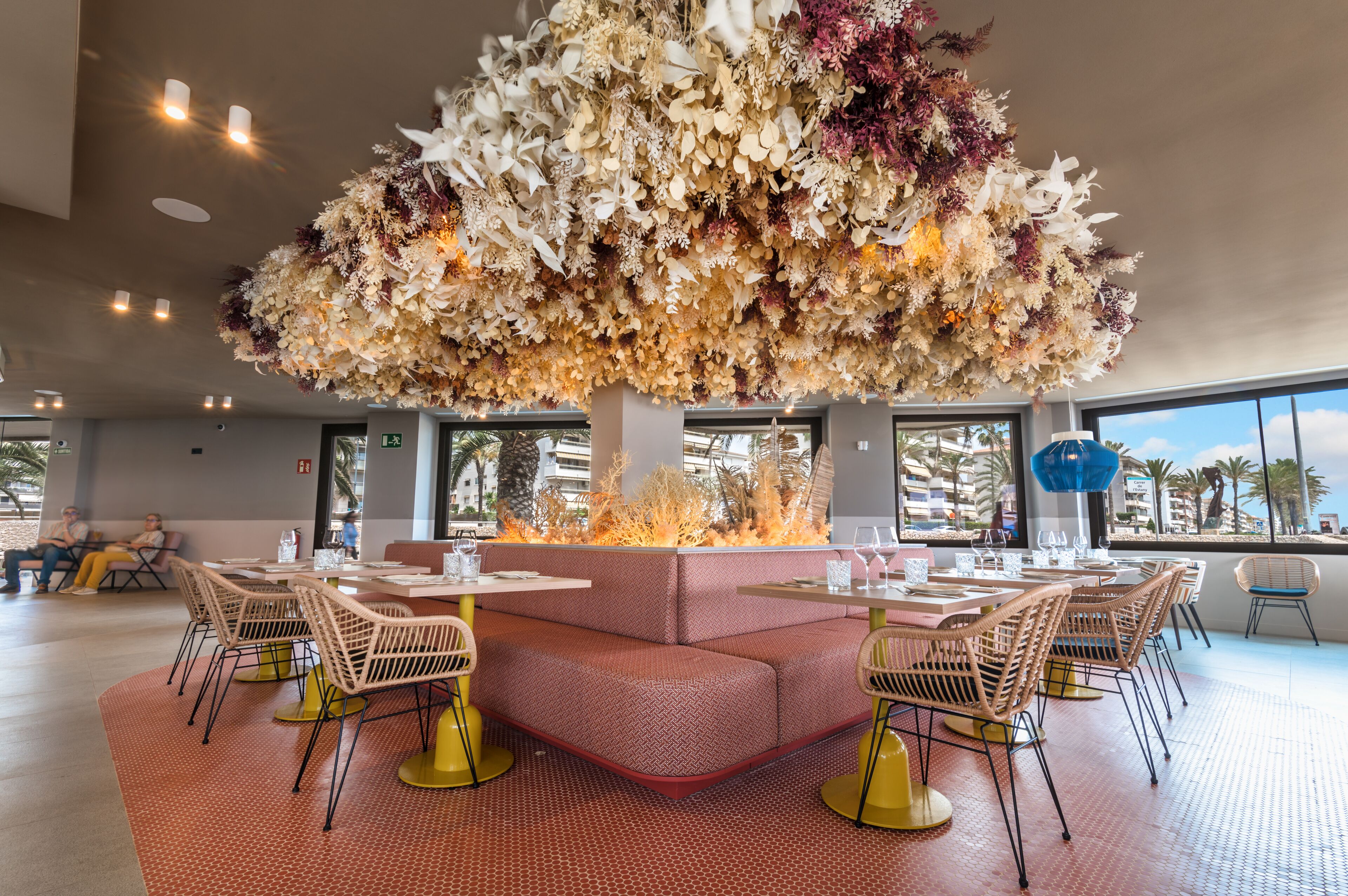A restaurant with a central fire feature, cushioned seating, and a view of palm trees.
