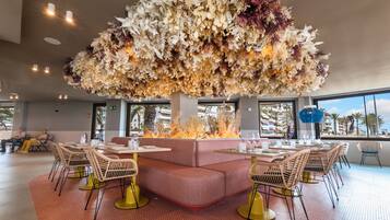 A restaurant with a central fire feature, cushioned seating, and a view of palm trees.