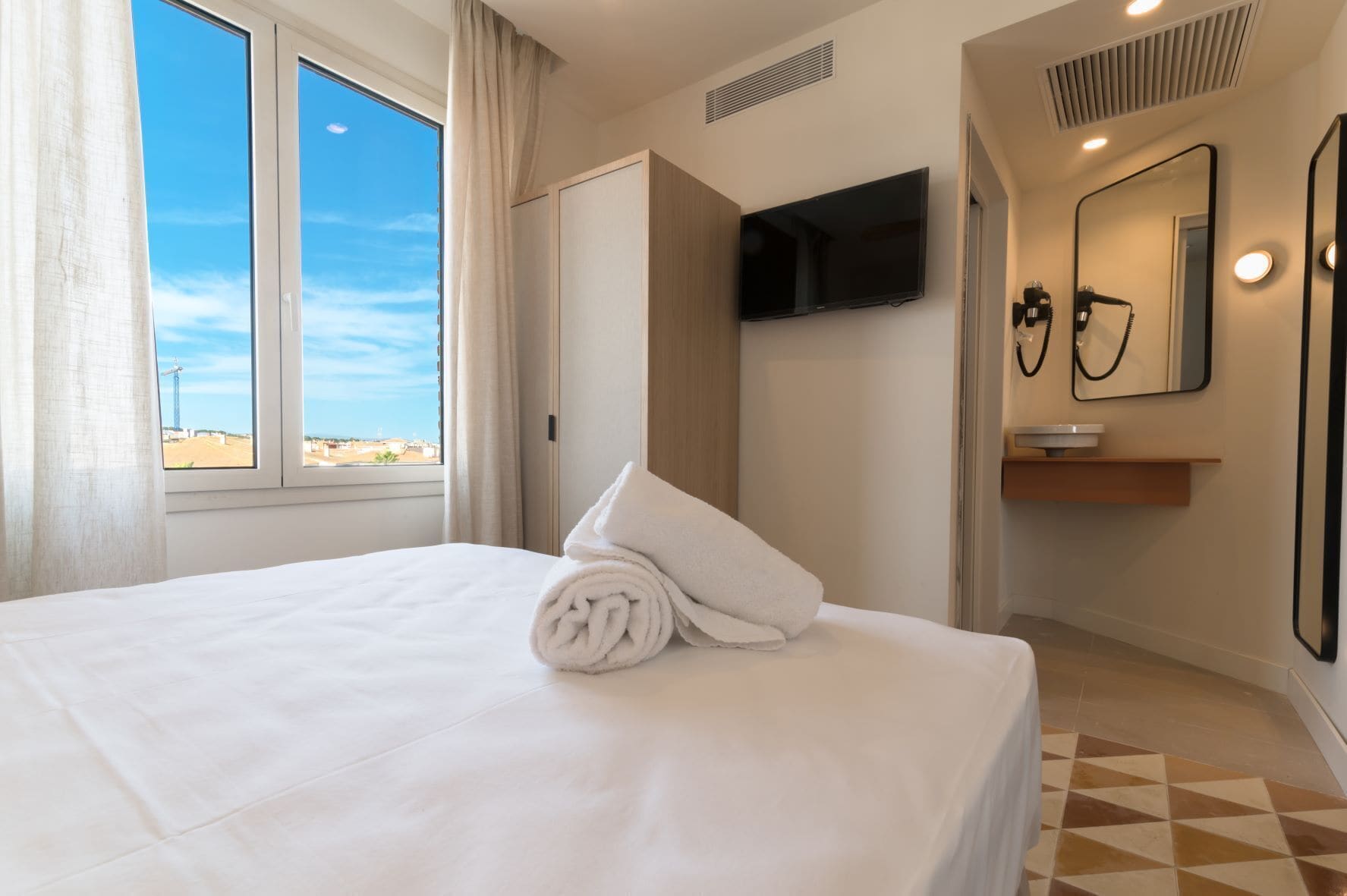 Een hotelkamer met een bed, een televisie, een spiegel en een badkamer met een wastafel en handdoekrek.