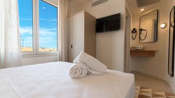 Habitación de hotel con cama, televisión, espejo y baño con lavamanos y toallero.