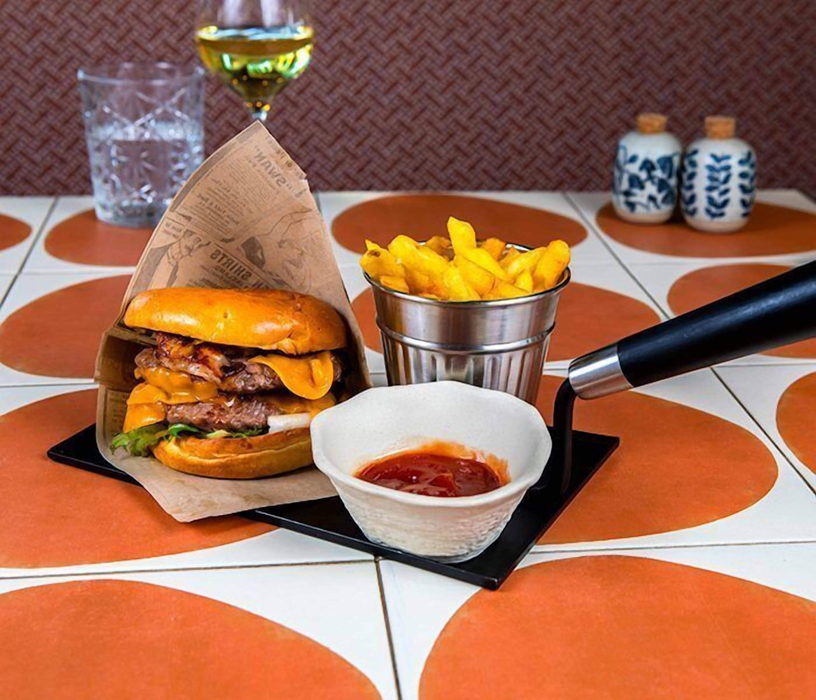 A meal consisting of a burger, fries, and ketchup, served on a table with a patterned tablecloth.