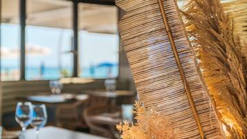 A restaurant interior with a table set for dining, a decorative woven centerpiece, and a view of the sea through large windows.