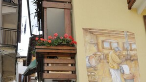 Une rue étroite ornée d’une fresque représentant une femme en train de cuisiner, de pots de fleurs et d’une structure en bois.