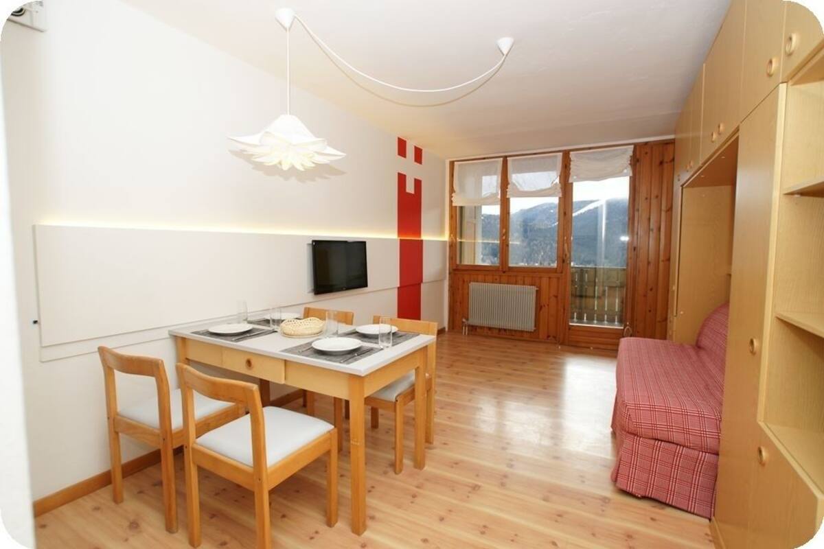 A compact living space with a dining area, a TV mounted on the wall, and a window with a view of the outdoors.