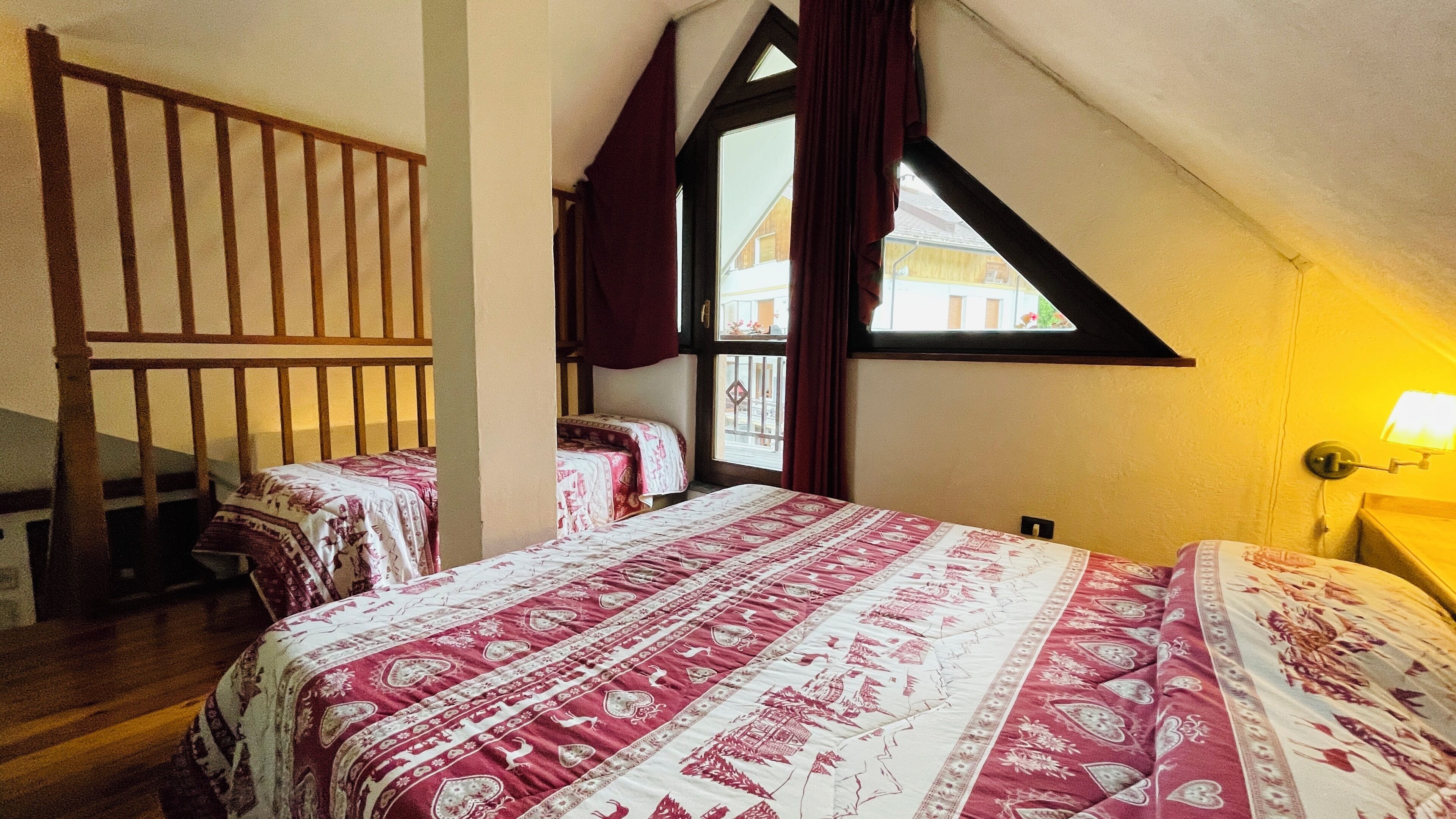 A bedroom with two beds, a wooden staircase, and a window with curtains.