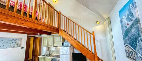 A kitchen with a wooden staircase, a refrigerator, a microwave, and a dining area with chairs.