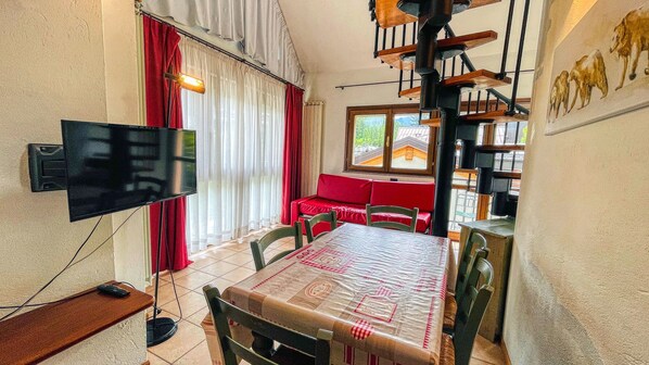A dining area with a table, chairs, a TV, and a red sofa. - Residence villa Frejus (Bardonecchia)