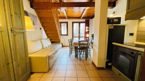 A cozy kitchen with a wooden ceiling, a dining area with a table and chairs, and a built-in stove. - Residence villa Frejus (Bardonecchia)