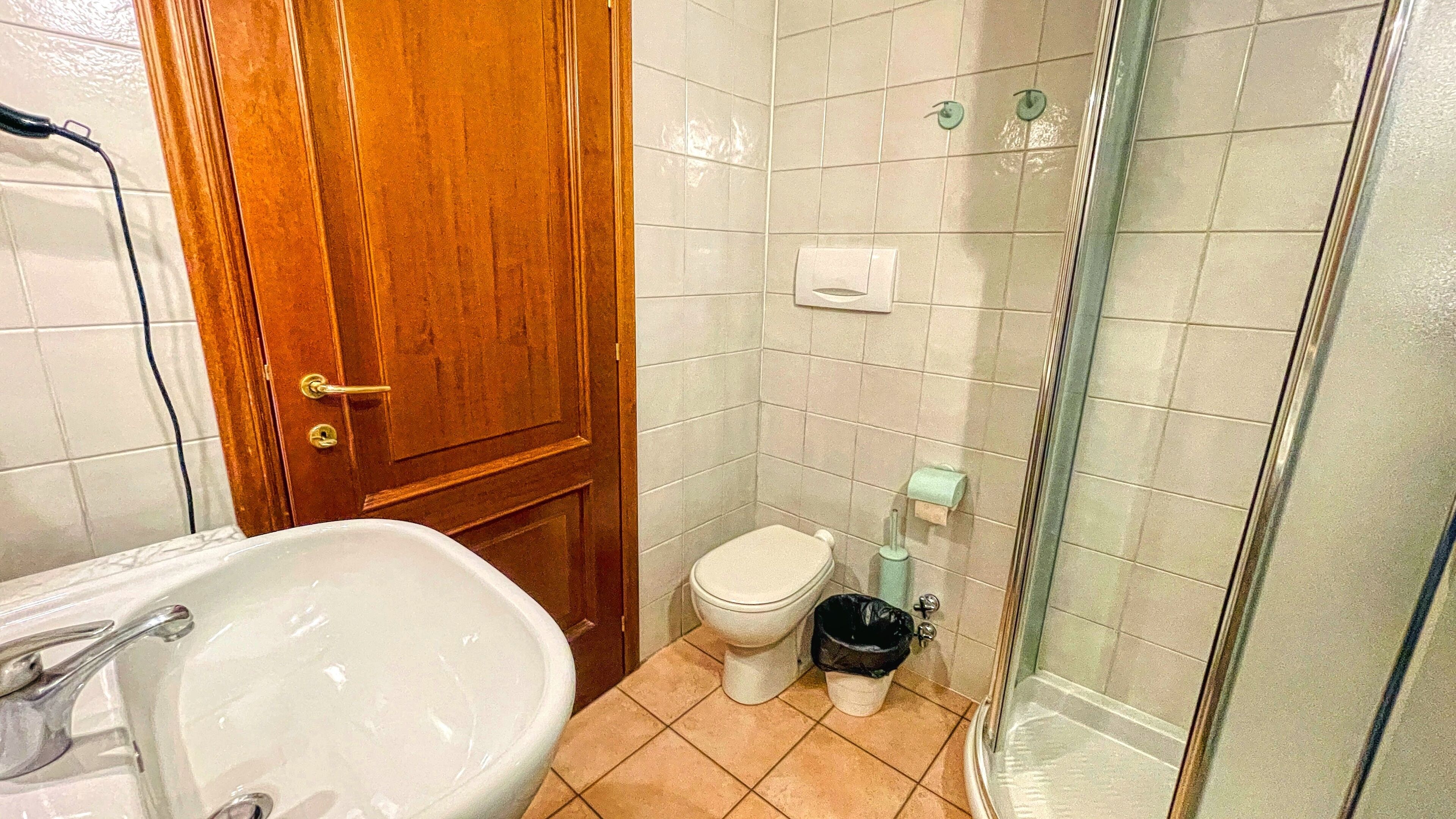A bathroom with a wooden door, white tiles, a sink, a toilet, and a shower area.