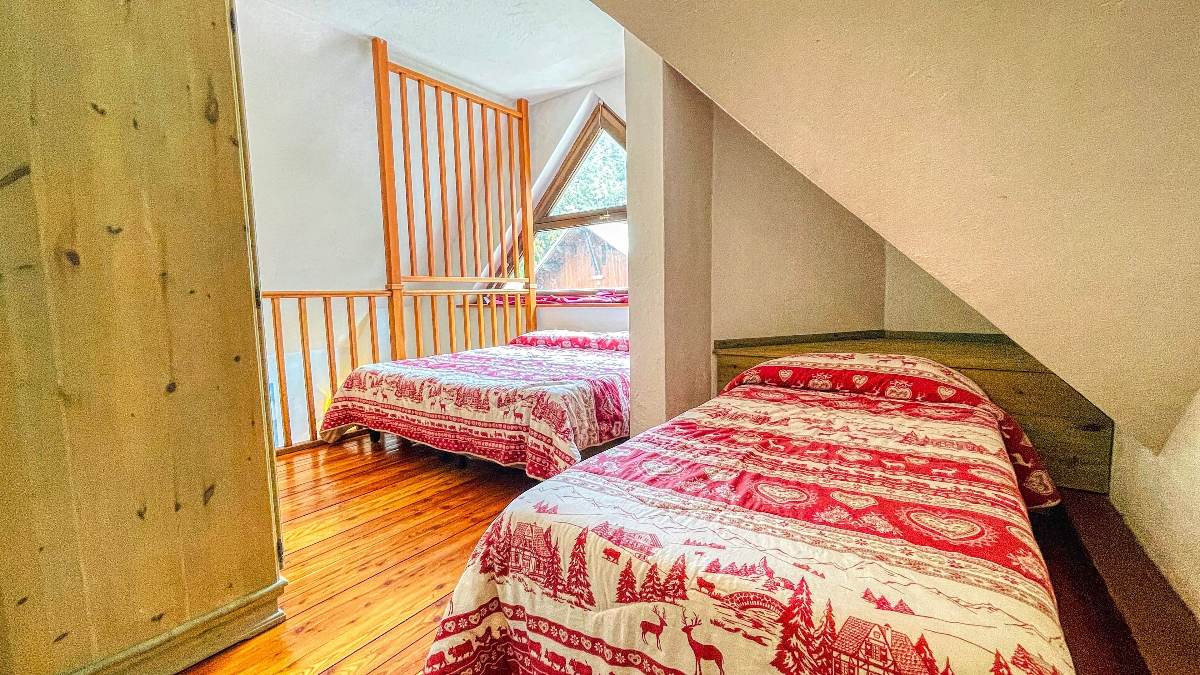 A bedroom with two beds, wooden flooring, and a sloped ceiling.