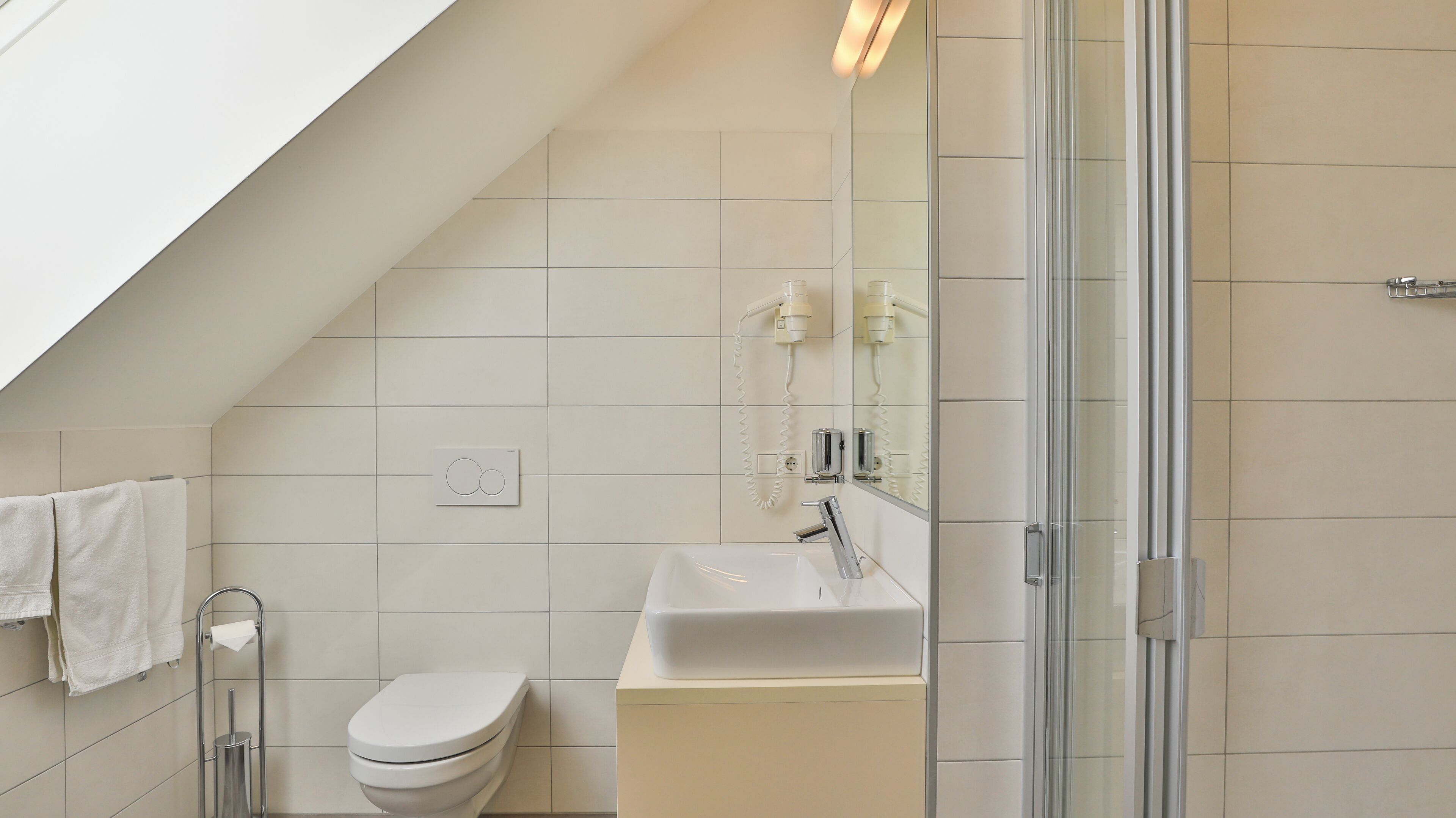 Een moderne badkamer met een schuine plafond, een toilet, een wastafel en een douchecabine van glas.
