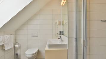 Een moderne badkamer met een schuine plafond, een toilet, een wastafel en een douchecabine van glas.