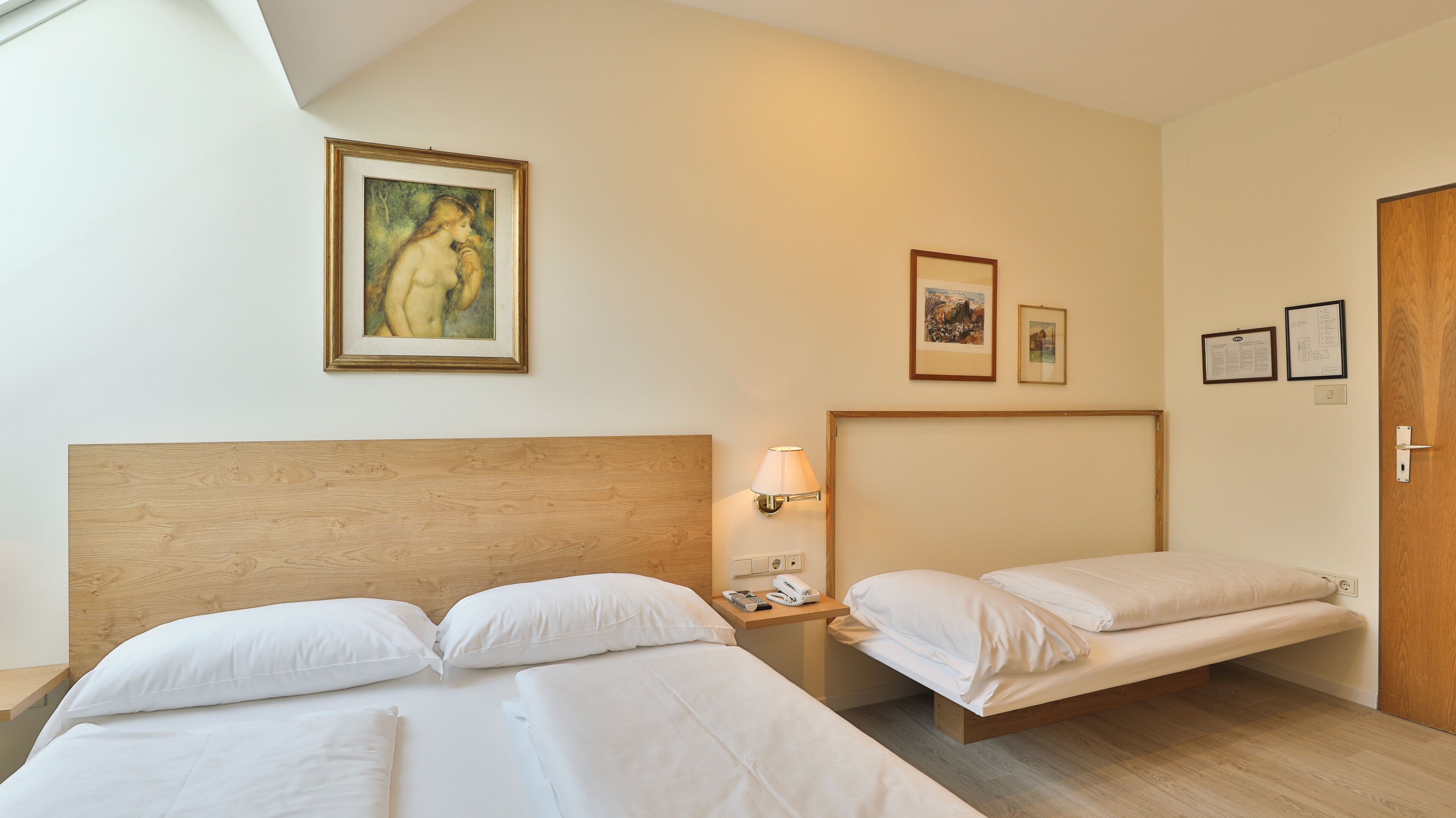Une chambre d’hôtel avec deux lits, une tête de lit en bois, une lampe de chevet et des œuvres d’art encadrées accrochées aux murs.