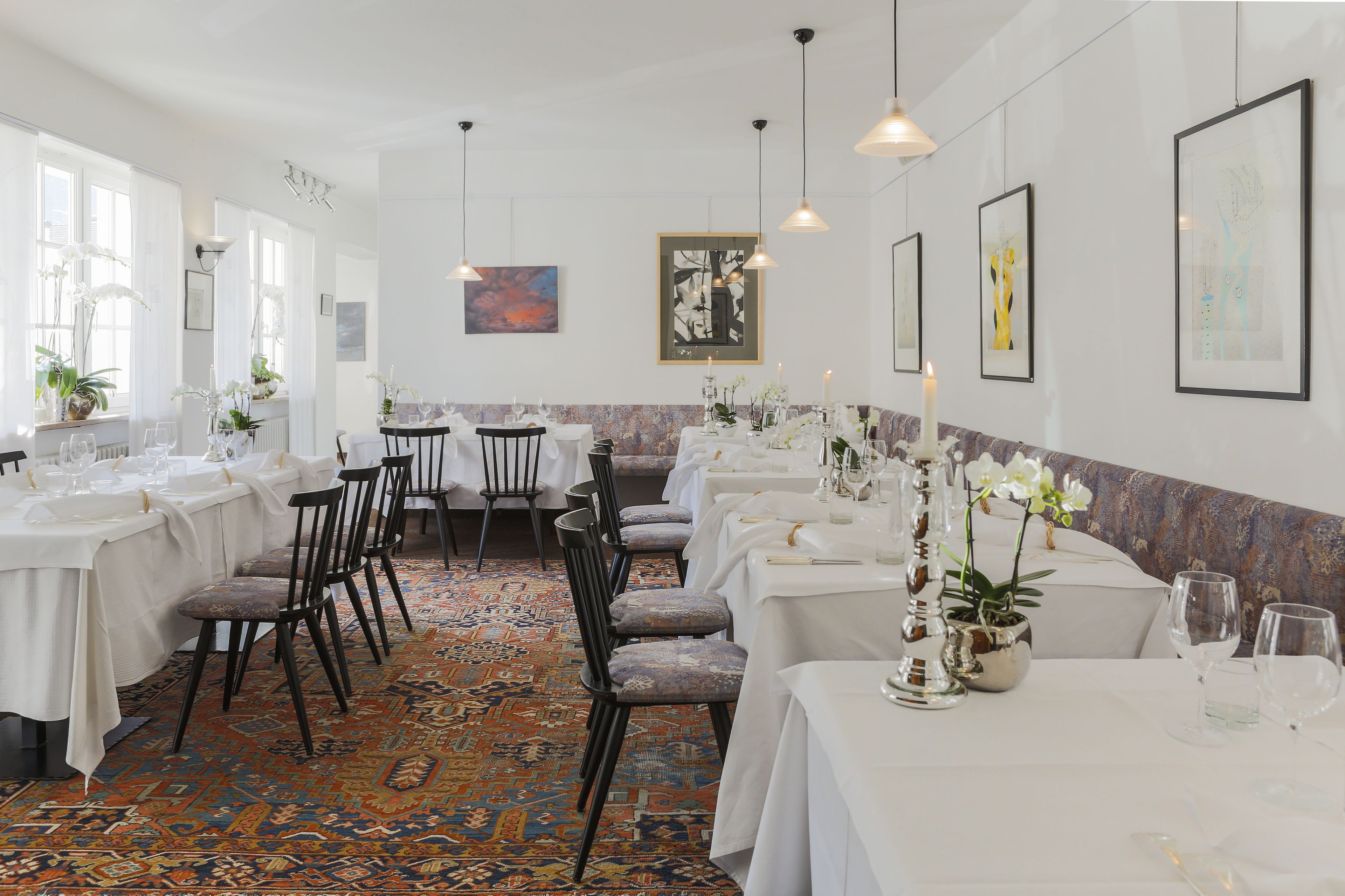 A dining area with multiple tables set for service, chairs, and hanging pendant lights.