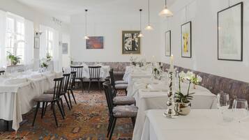 A dining area with multiple tables set for service, chairs, and hanging pendant lights.
