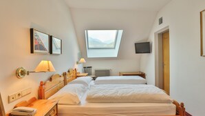 Una habitación de hotel con dos camas, un tragaluz, un televisor y un escritorio.