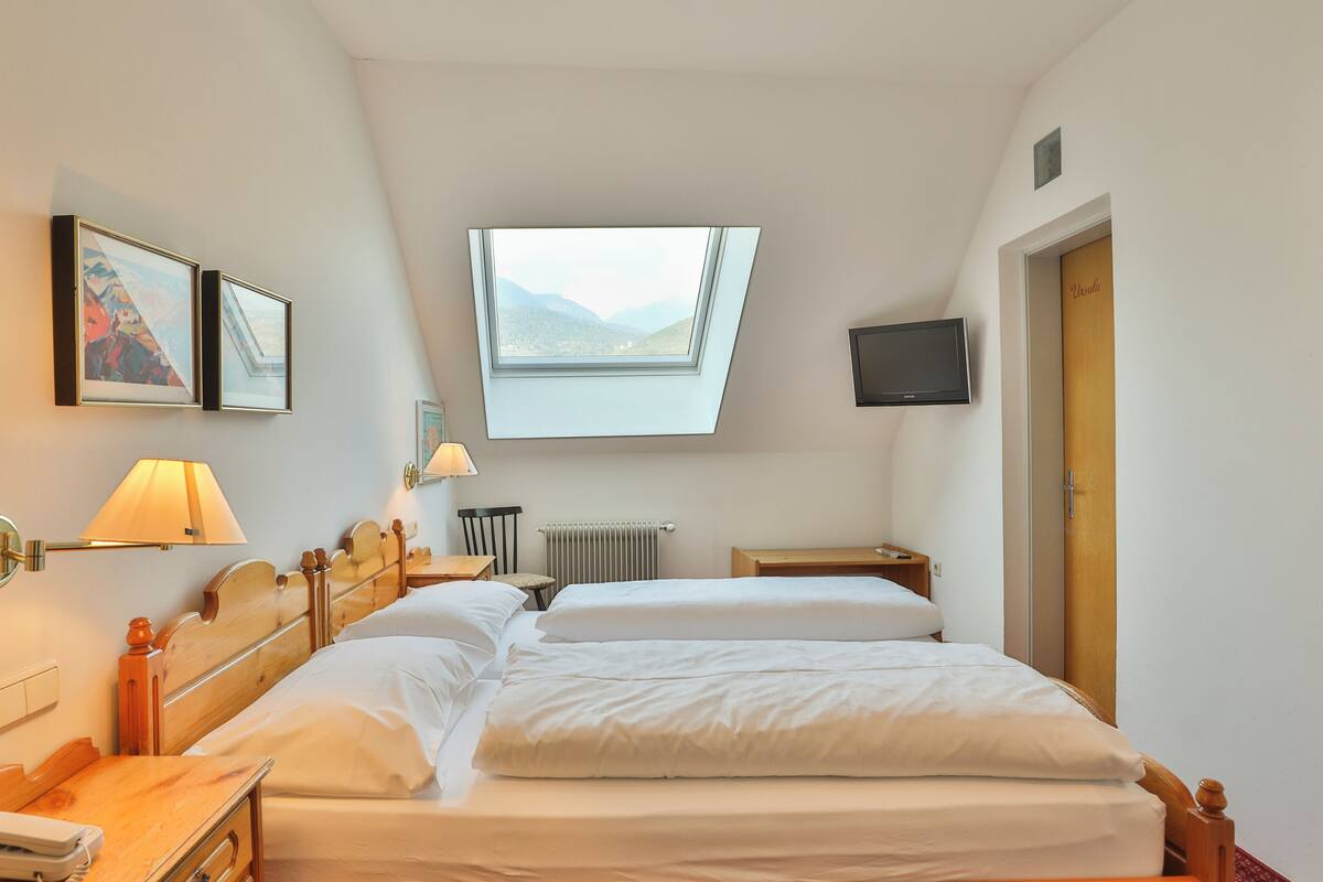 A hotel room with two beds, a skylight, a TV, and a desk.