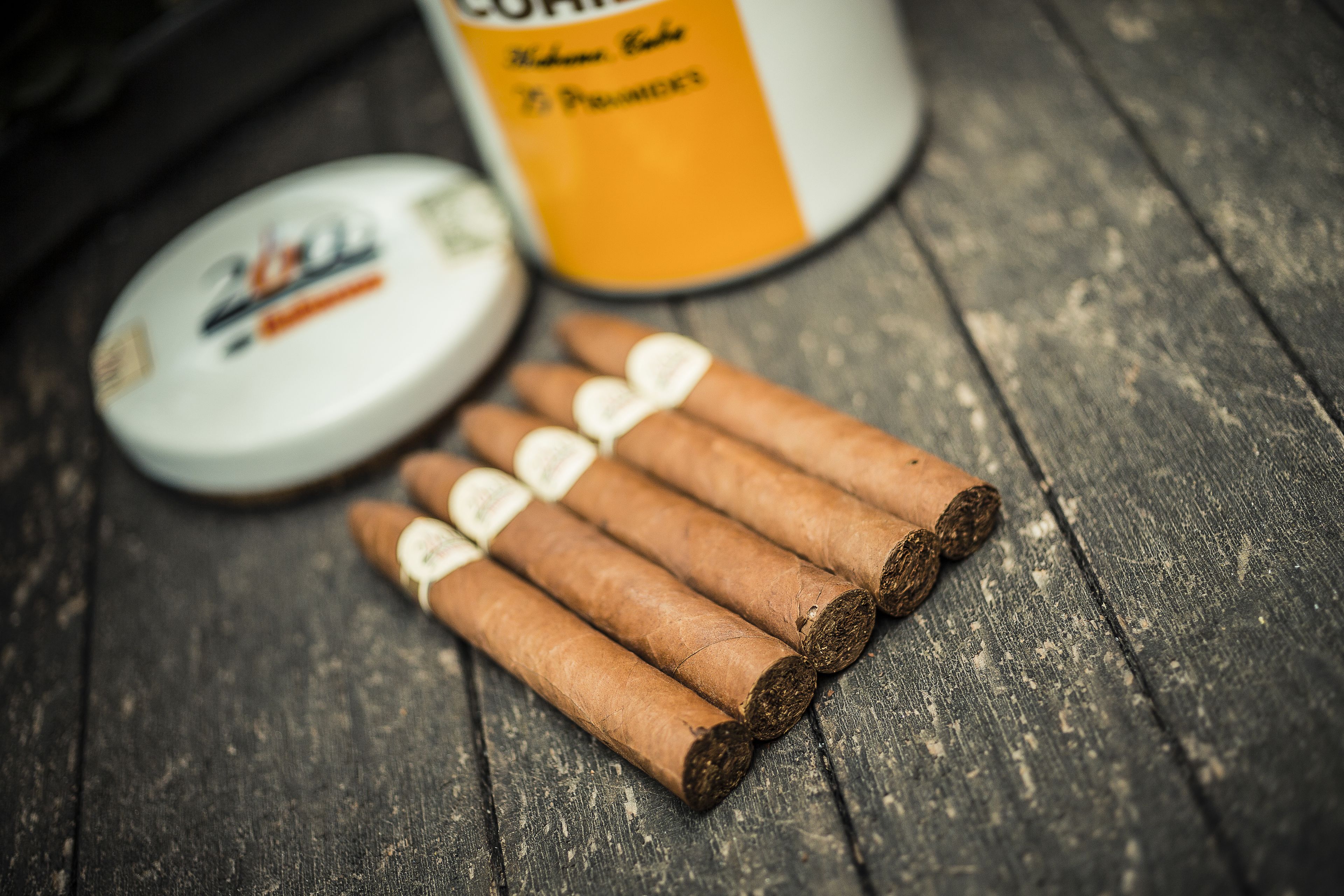 A wooden surface with five cigars and a tin of tobacco.