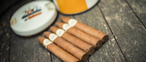 A wooden surface with five cigars and a tin of tobacco.