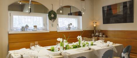 A dining area with a long table set for a meal, wooden beams on the ceiling, and a large abstract painting on the wall.