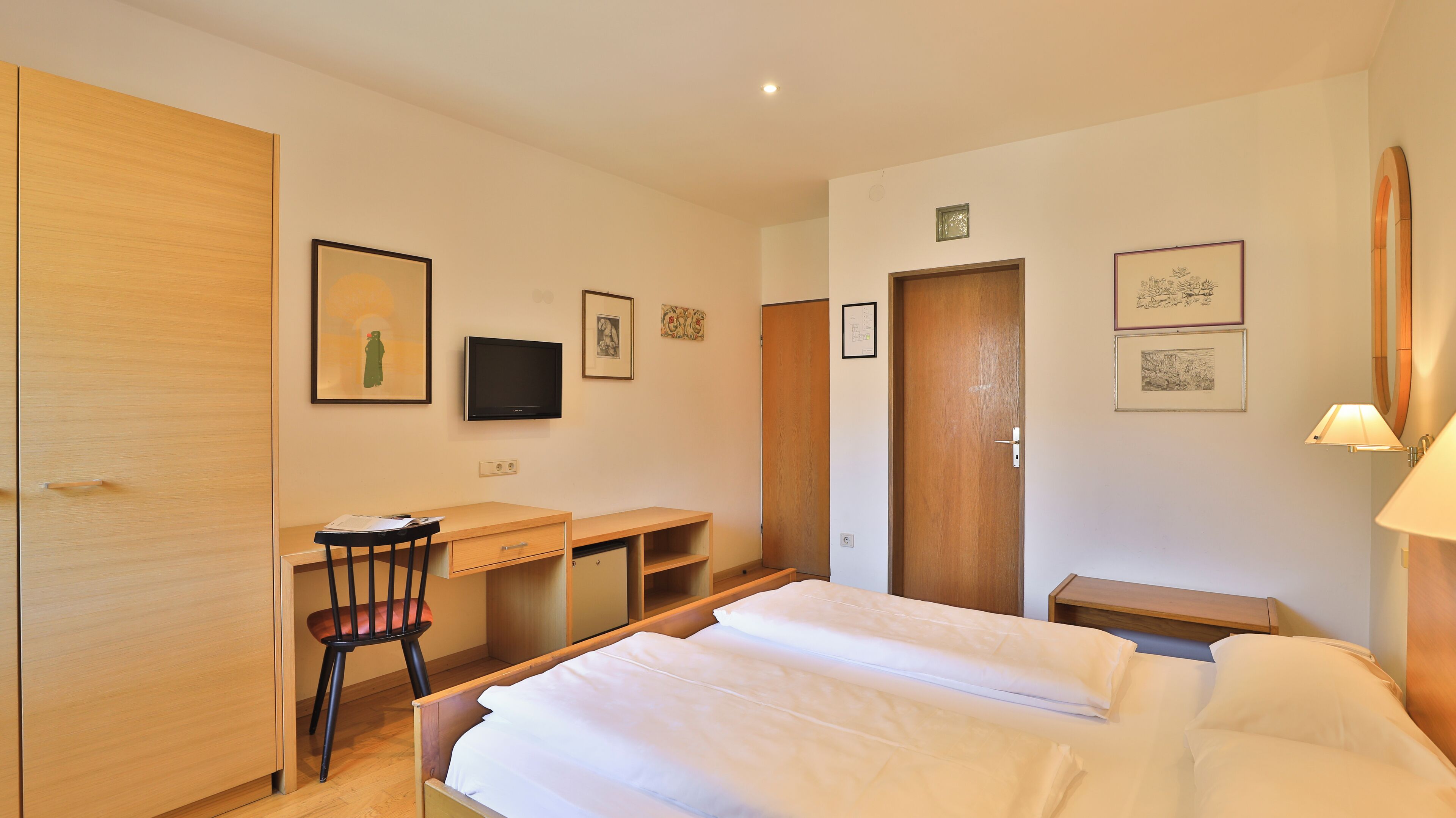 A hotel room with a bed, desk, chair, and a TV.