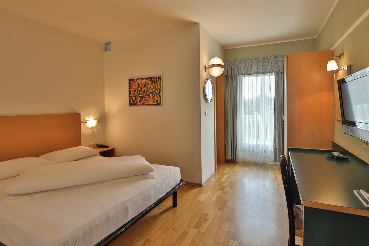 A hotel room with a bed, a desk, a TV, and a window with curtains.