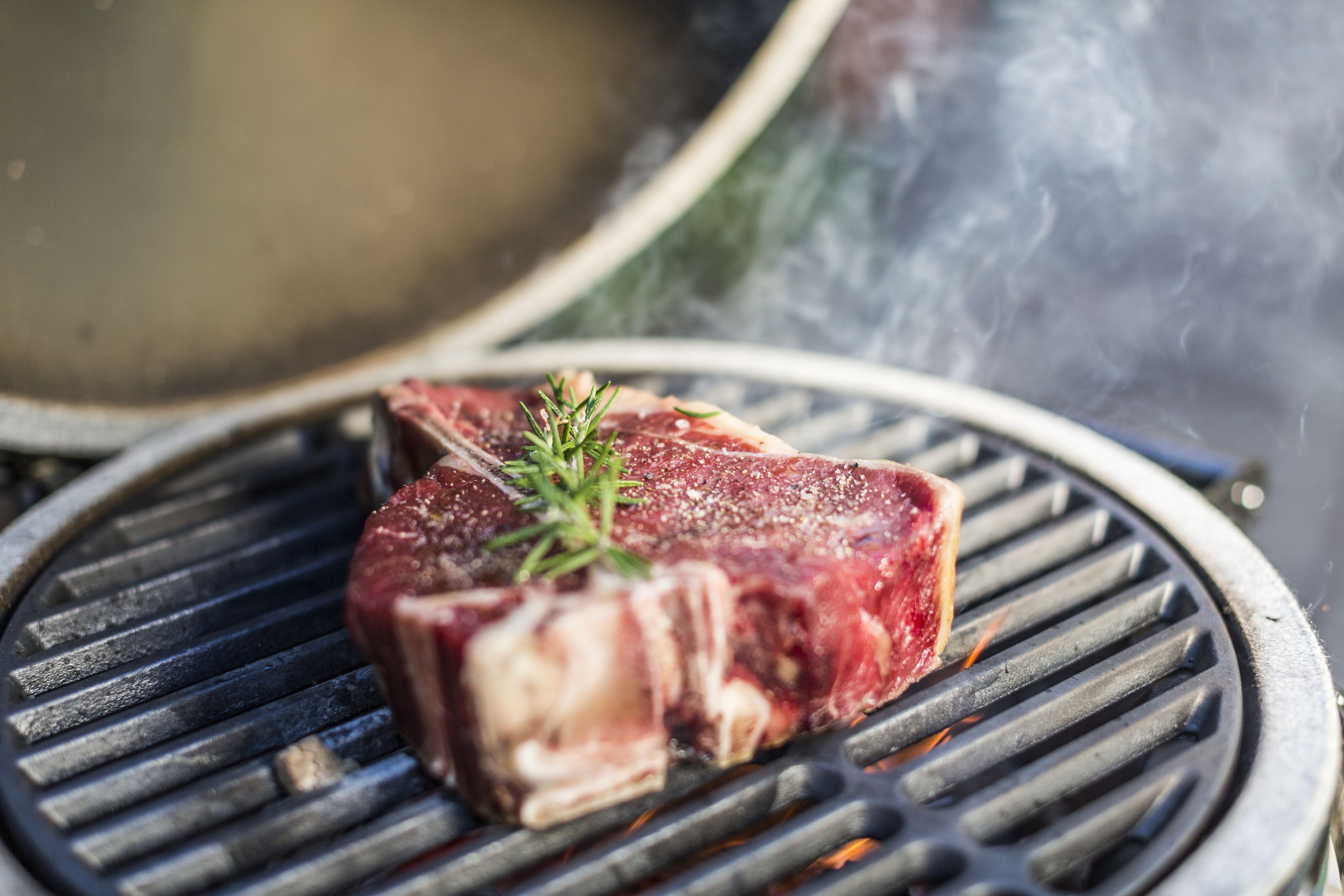Een steak op een grill met duidelijke grillstrepen en een takje rozemarijn erbovenop.