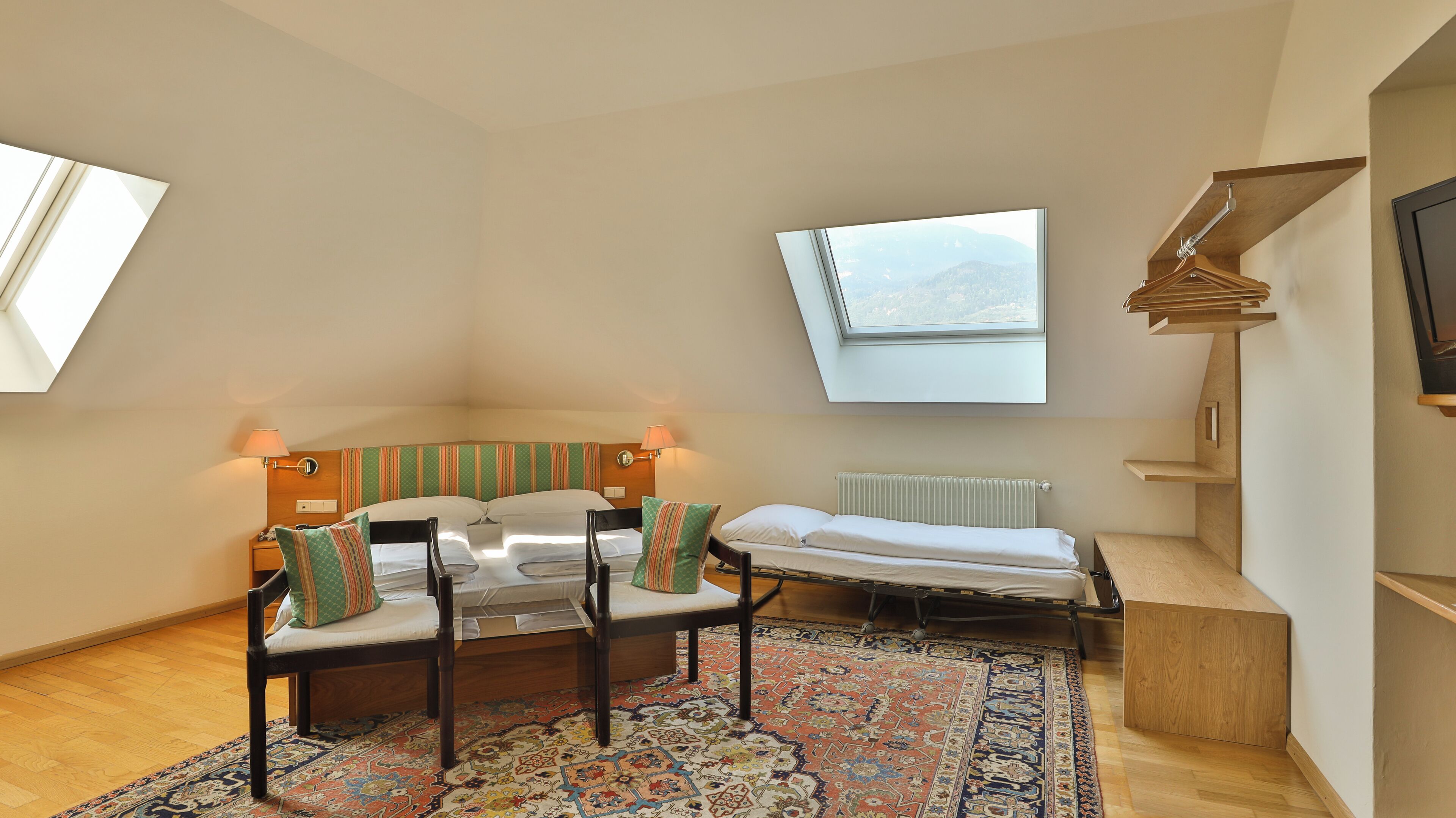 Un dormitorio con una cama, una silla, una mesita, un radiador y una ventana con vistas a las montañas.