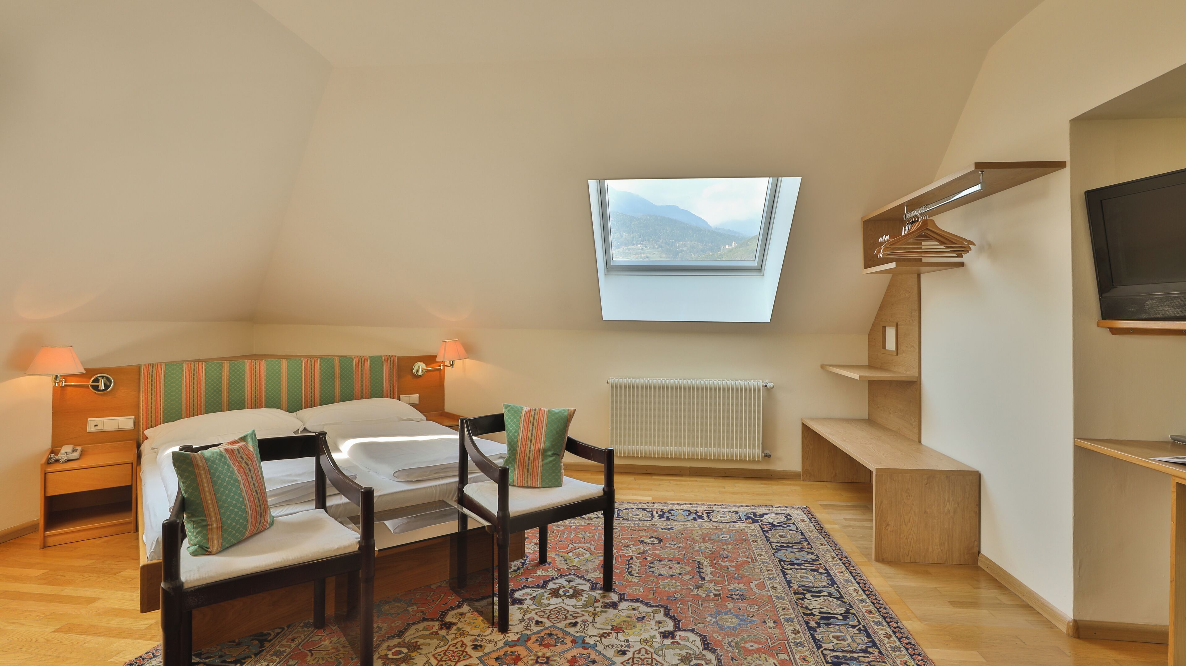 Ein Hotelzimmer mit einem Bett, zwei Nachttischen, einem Sessel, einem Fernseher, einem Fenster und einer Heizung.