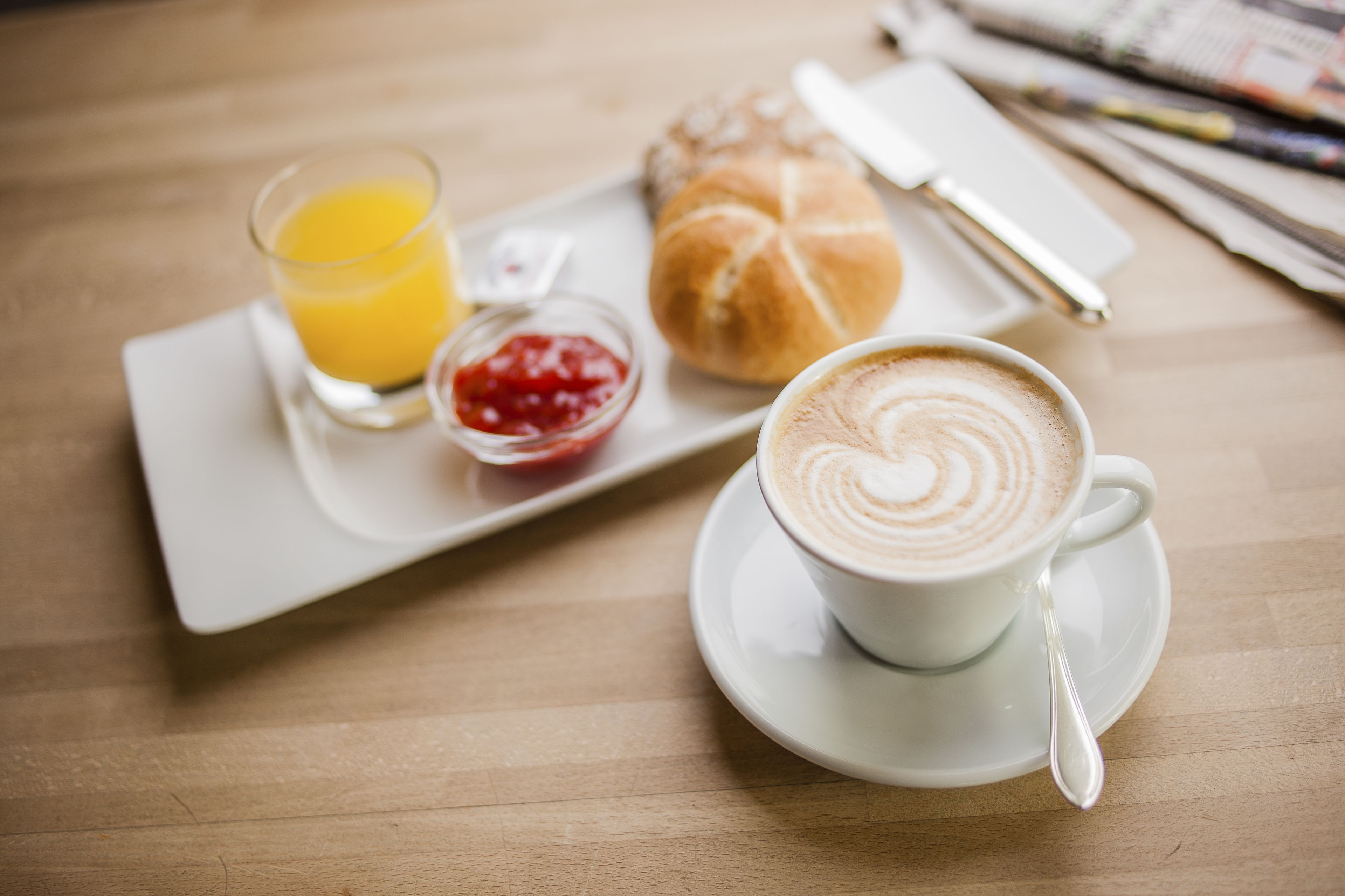 Ein Frühstücksbrett mit einer Kaffeetasse, einem Orangensaftglas, einem Croissant und einer kleinen Marmeladengläschen.