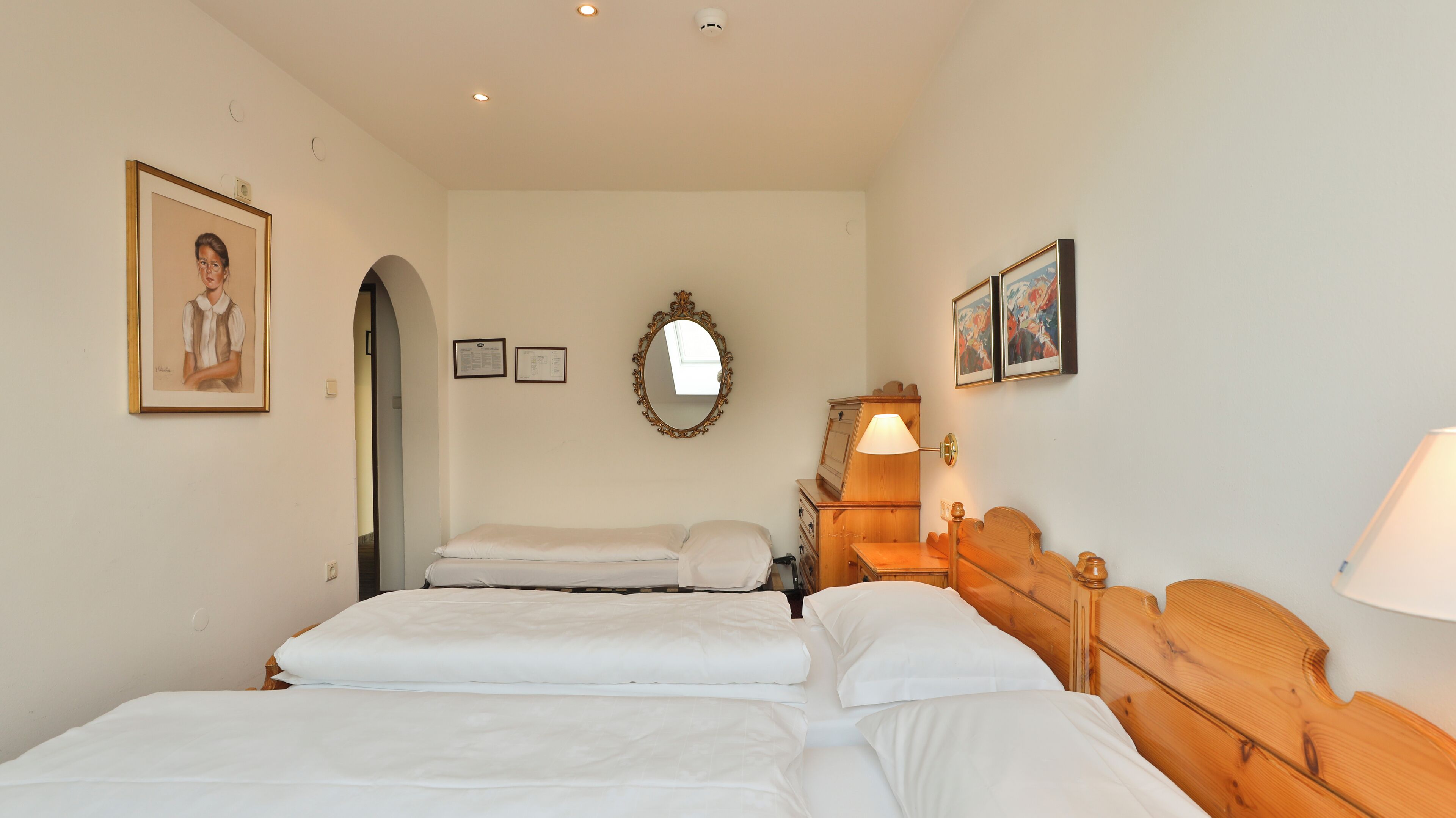 A hotel room with a double bed, a wooden nightstand with a lamp, a mirror, and framed artwork on the walls.