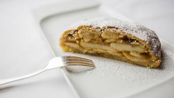 A slice of apple strudel on a white plate with powdered sugar, accompanied by a fork.