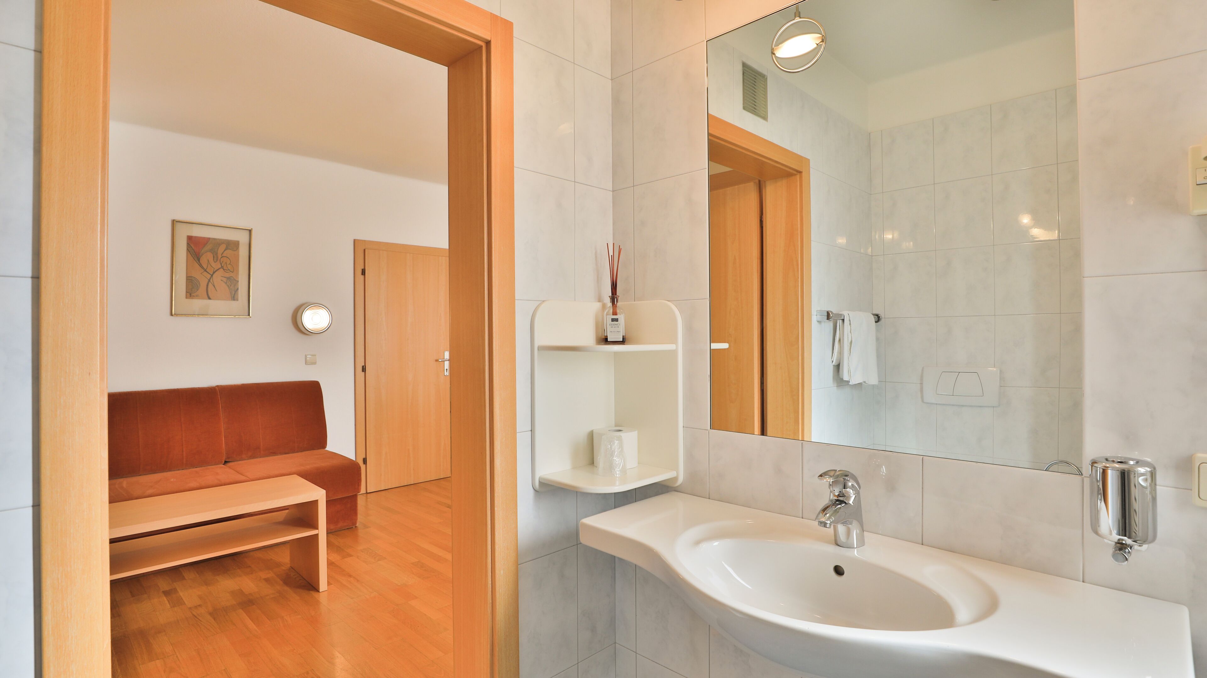 Un bagno moderno con un lavandino bianco, uno specchio e una porta in legno.