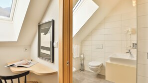 A modern bathroom with a toilet, sink, and shower. There is a skylight above the toilet and a framed picture on the wall. - Hotel Sparerhof (Terlano)
