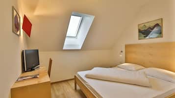 A hotel room with a bed, a desk with a computer, a chair, a window, and a painting on the wall.