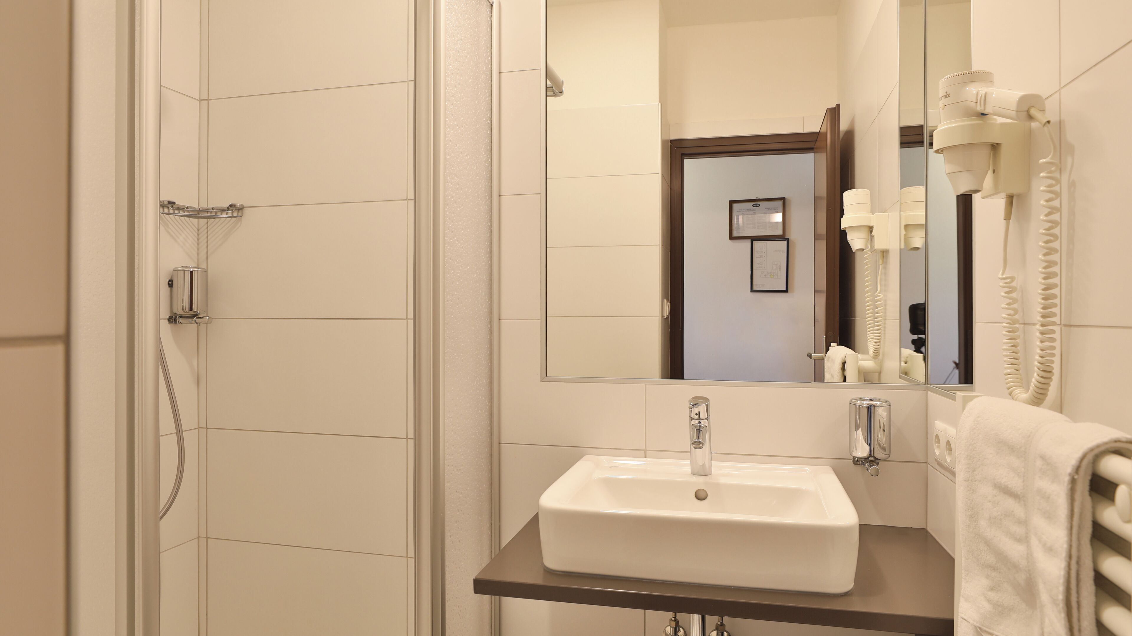 A bathroom with a shower, a sink, and a hairdryer mounted on the wall.